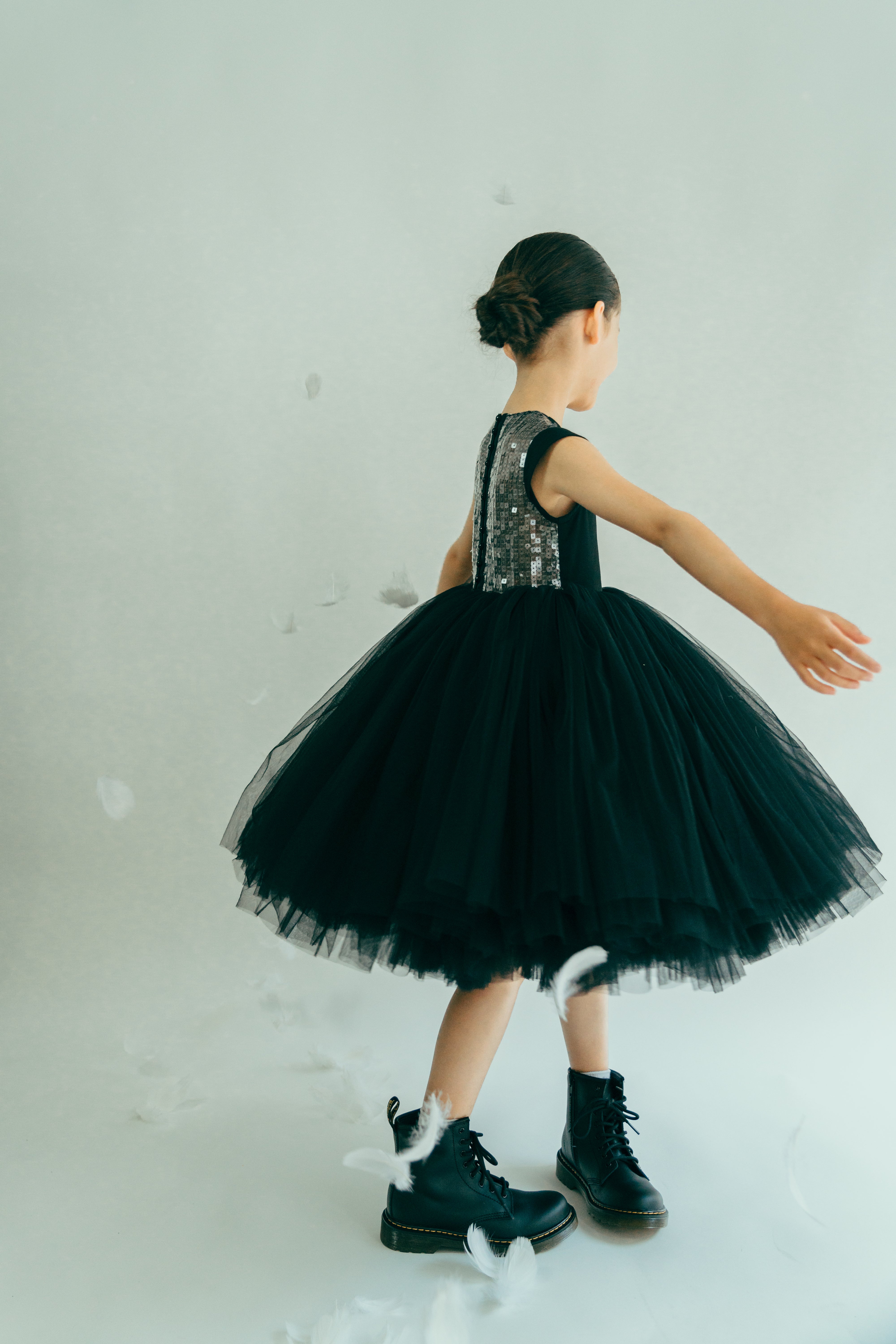Girl twirling in white feathers wearing a black tulle dress with silver back