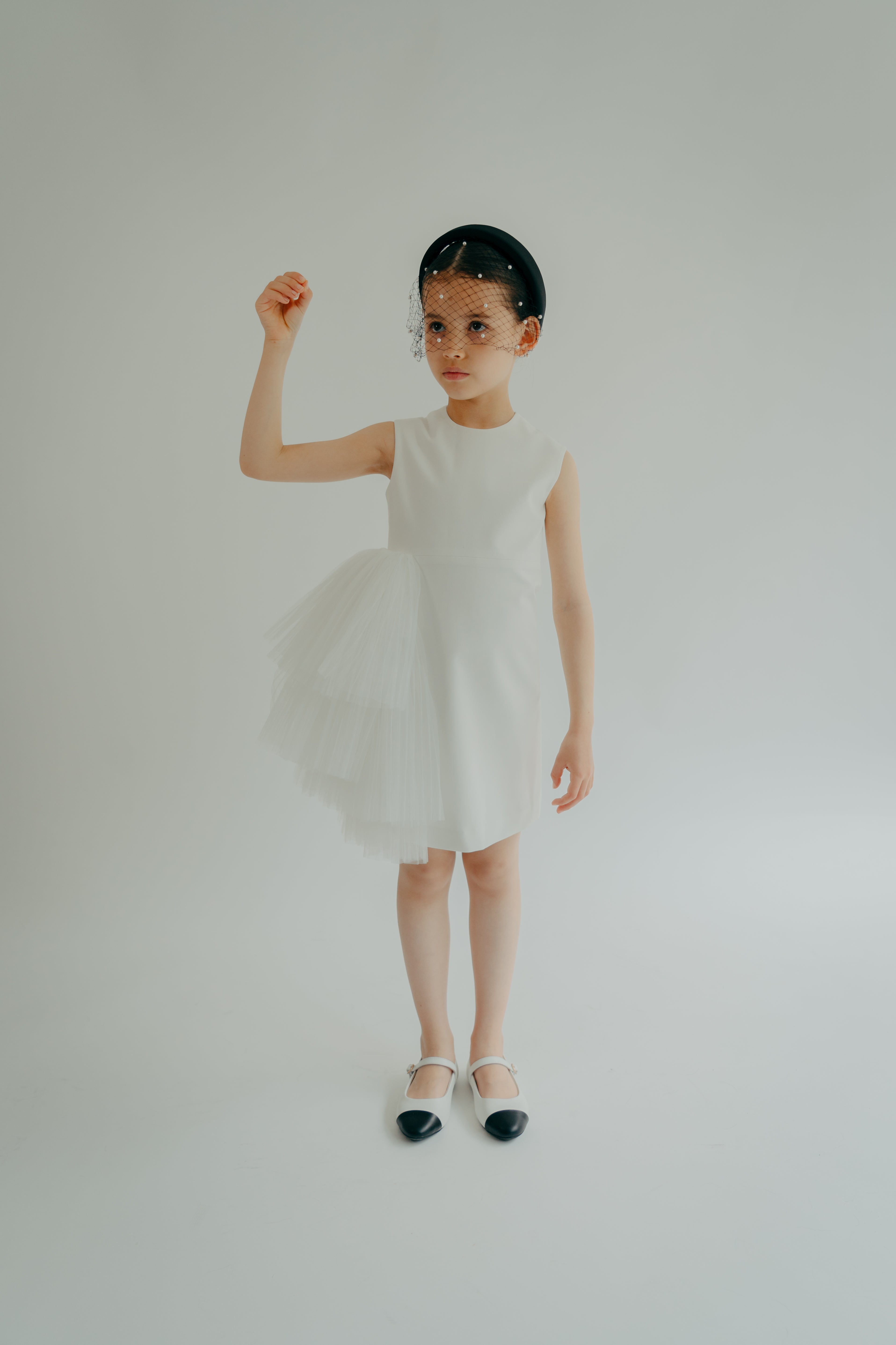 A young child in a white sleeveless dress with 3D tulle ruffles on the sides