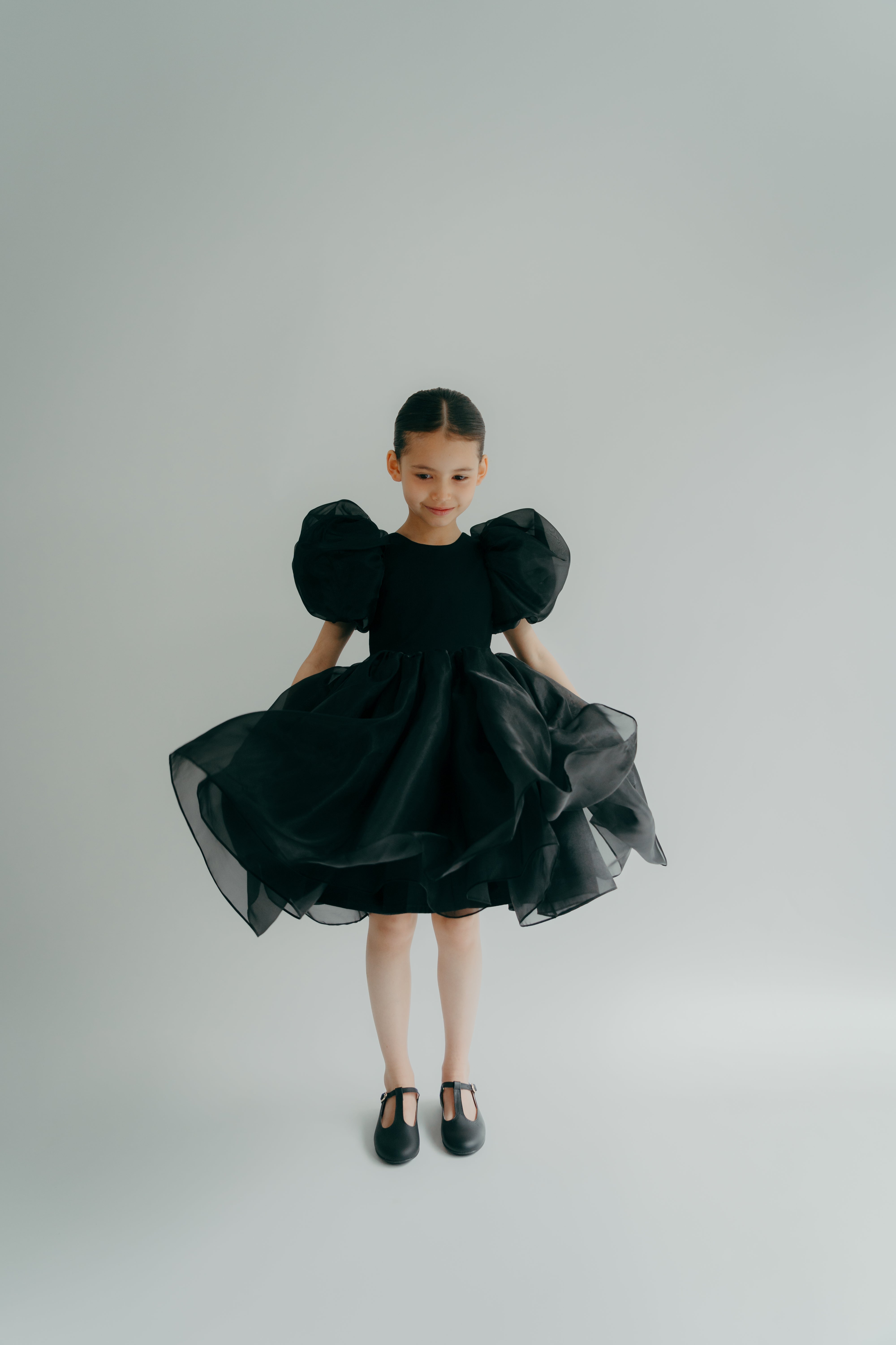 A young child wearing a black dress with puff sleeves and a full skirt.