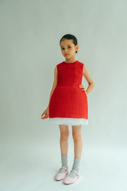 A young girl wearing a red sleeveless knee-length dress with white tulle at the hem